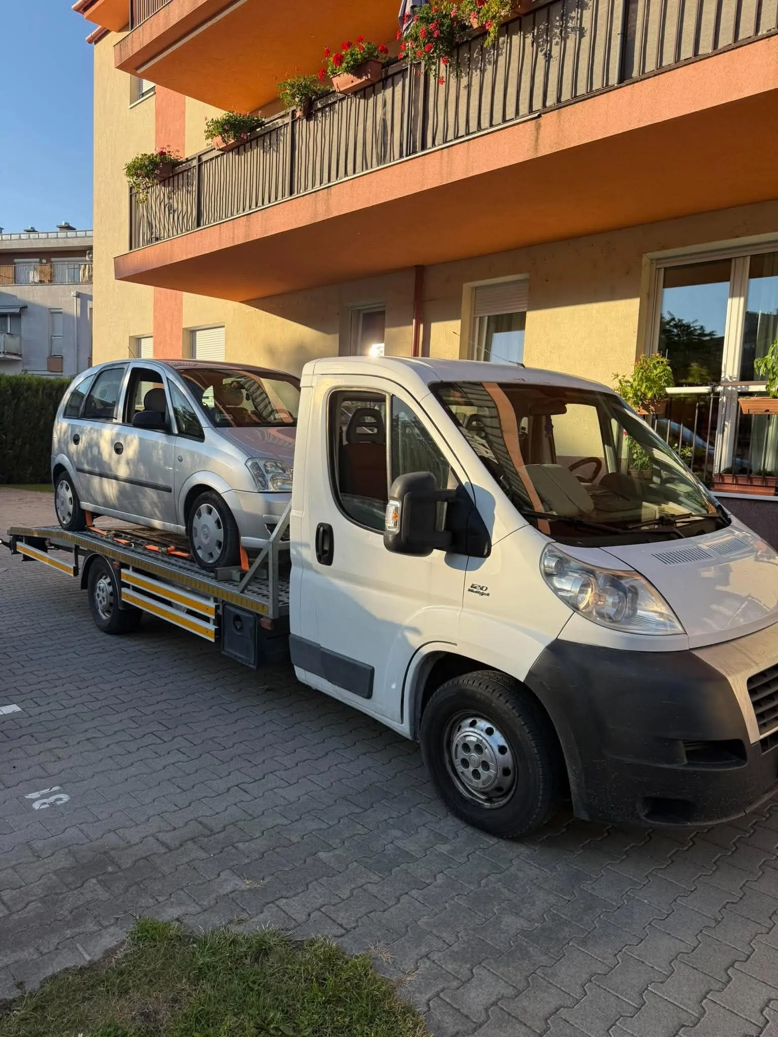 Ezüst autó felrakva a vontatóra egy lakóház előtt